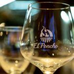 Copa de vino con logotipo de El Poncho en primer plano dentro del restaurante.