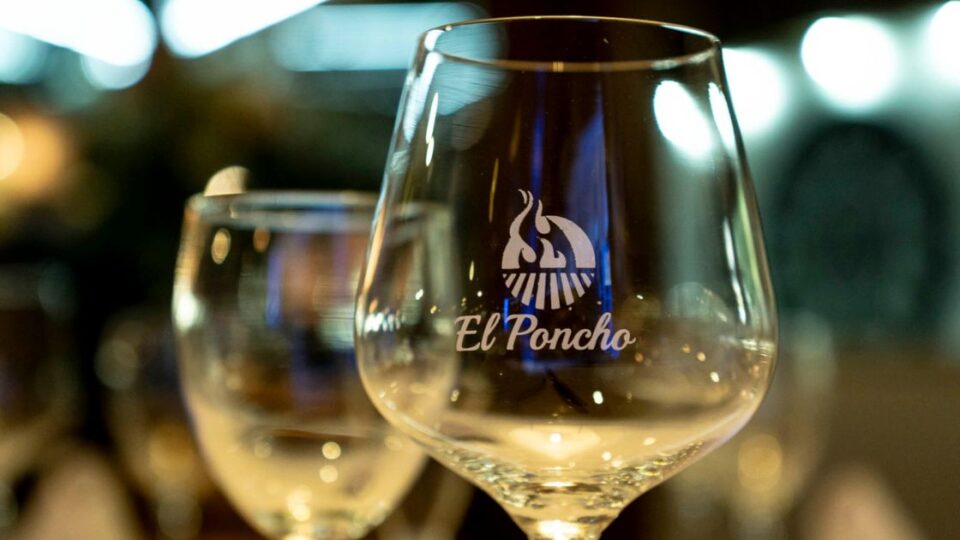Copa de vino con logotipo de El Poncho en primer plano dentro del restaurante.