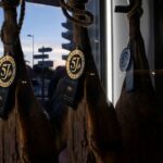 Jamones ibéricos colgados en el interior de El Poncho junto a ventanal exterior.