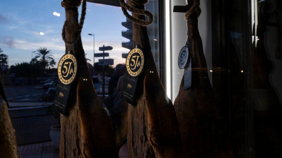 Jamones ibéricos colgados en el interior de El Poncho junto a ventanal exterior.