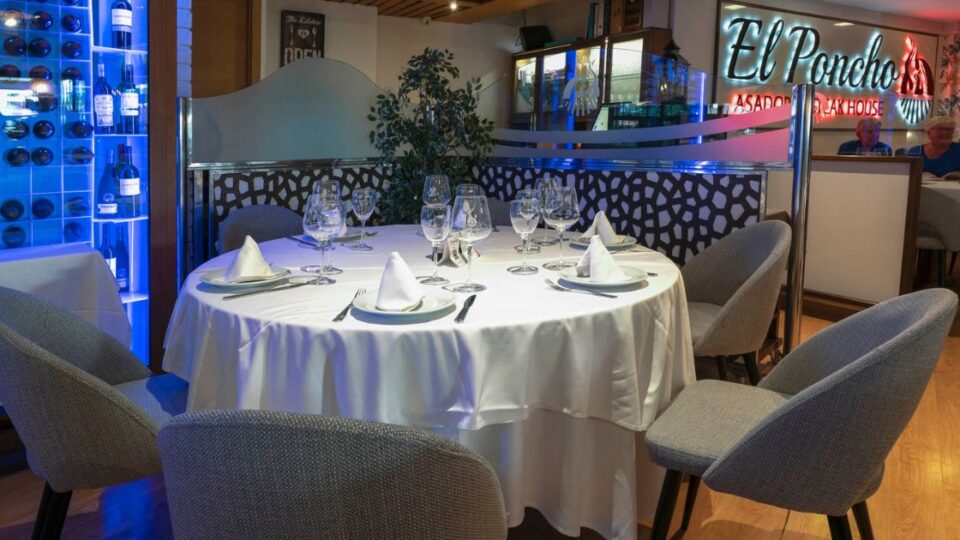 Sala interior del restaurante El Poncho con mesa redonda, vinoteca iluminada y zona de comensales.