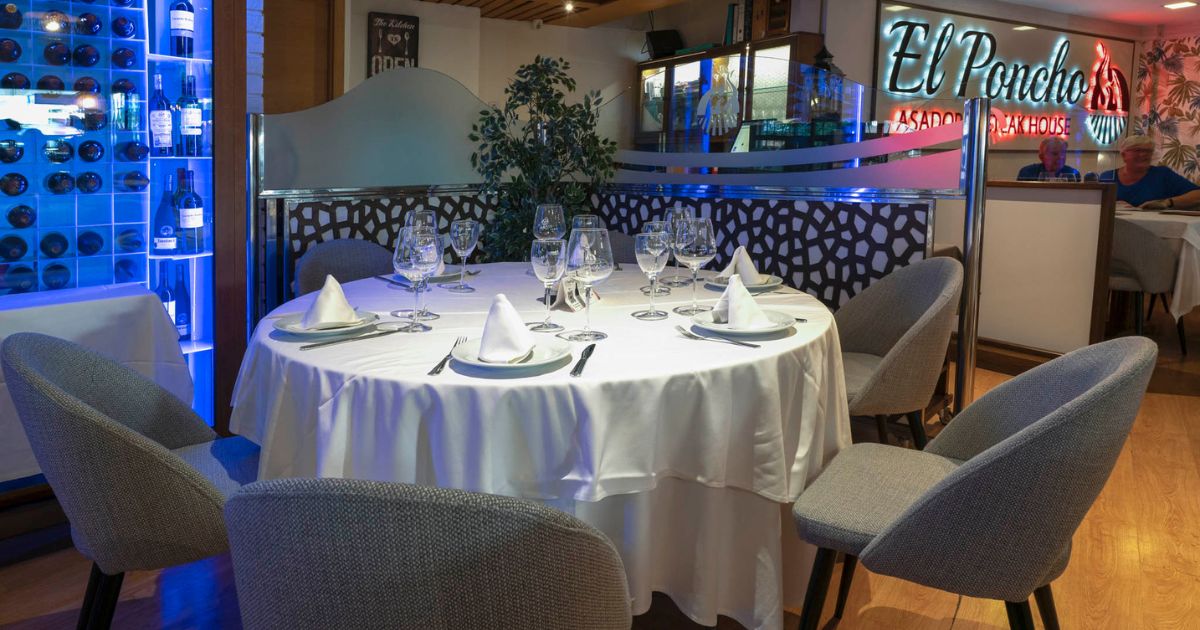 Sala interior del restaurante El Poncho con mesa redonda, vinoteca iluminada y zona de comensales.