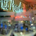 Vista interior del restaurante El Poncho con copas en primer plano y logotipo iluminado al fondo.