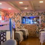 Zona interior del restaurante El Poncho con mesas reservadas y logotipo iluminado al fondo.