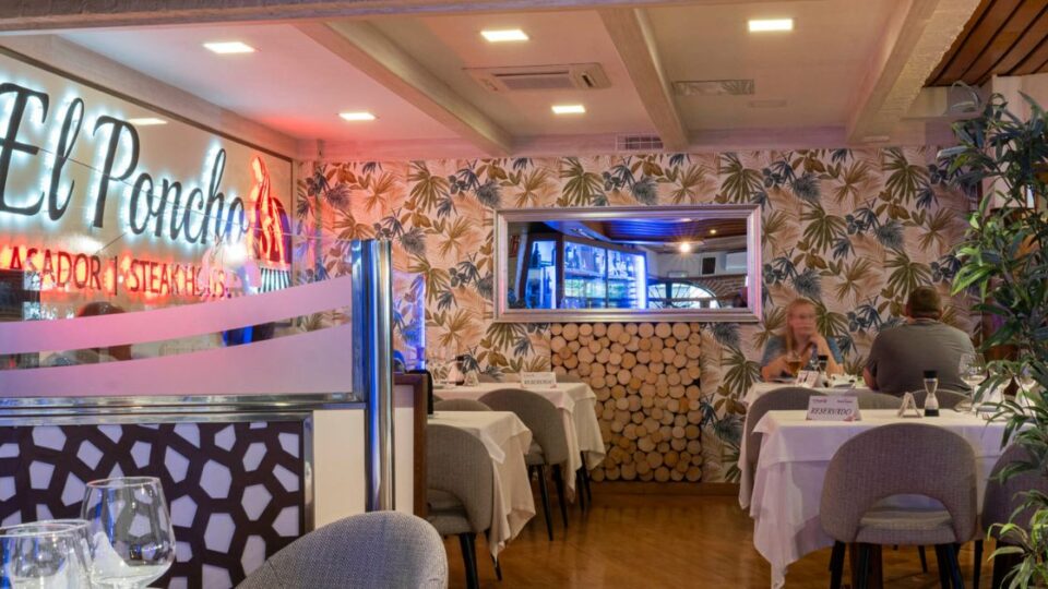 Zona interior del restaurante El Poncho con mesas reservadas y logotipo iluminado al fondo.